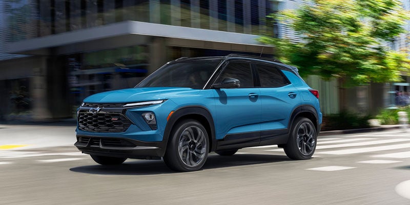 Blue Chevrolet Trailblazer RS SUV driving on a city street, with blurred buildings and trees in the background.