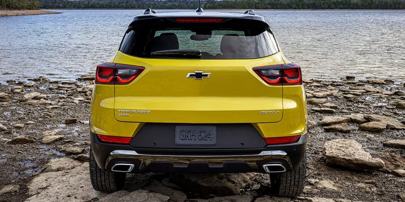 Rear view of a yellow Chevrolet Trailblazer SUV parked on a rocky shore next to a body of water.