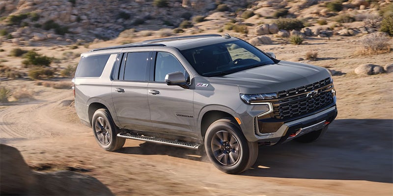 Gray Chevrolet Suburban Z71 SUV driving on a dirt road through a rocky desert landscape, wheels in motion.