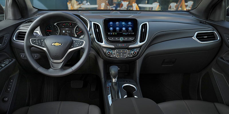 Interior view of a dark gray car, showing the steering wheel with a Chevrolet logo, dashboard, and infotainment screen.