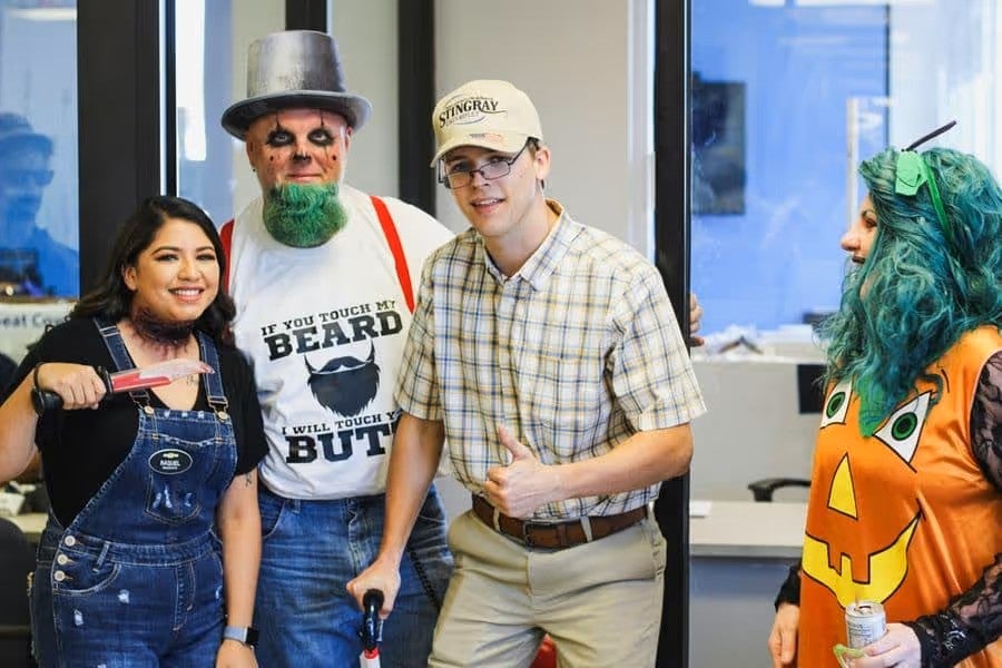 Group of people wearing Halloween-themed costumes and festive attire gathered indoors during a seasonal event