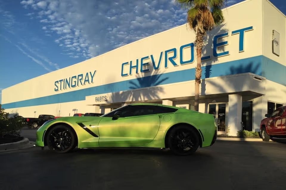 Vibrant green Corvette Stingray parked outside a white and blue Stingray Chevrolet dealership building.