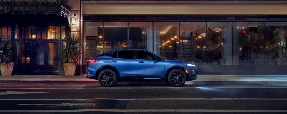 A blue Buick Envista is driving with their headlights on down a city street.