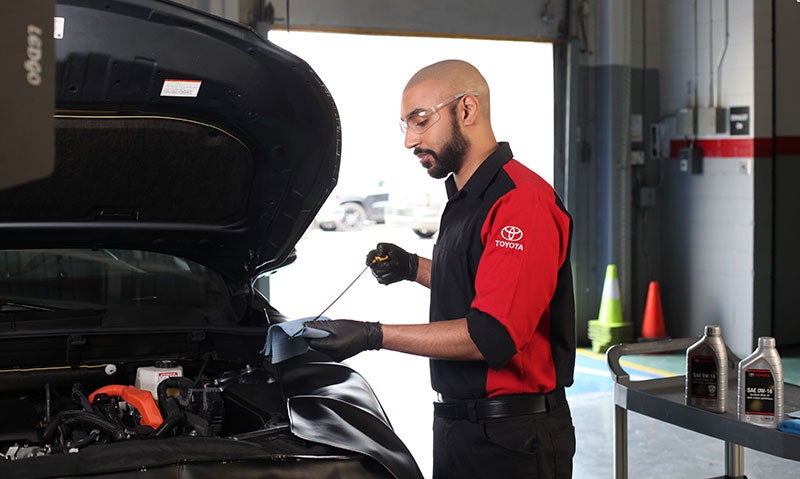 A professional in a red and black shirt is repairing a car, focused on the engine with tools in hand.