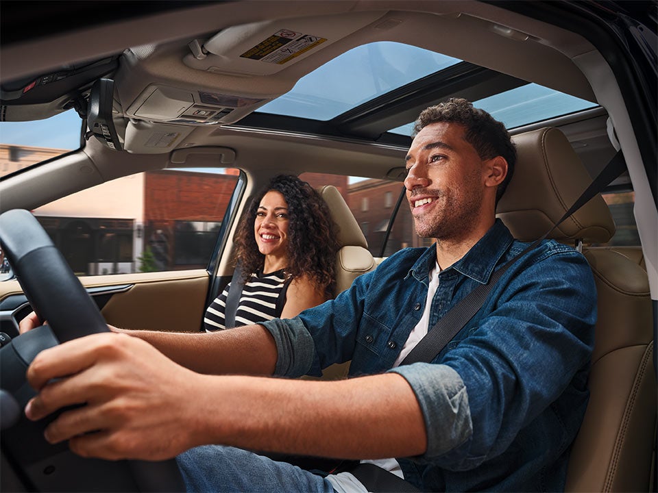 A smiling couple enjoys a drive in a modern car with a panoramic sunroof