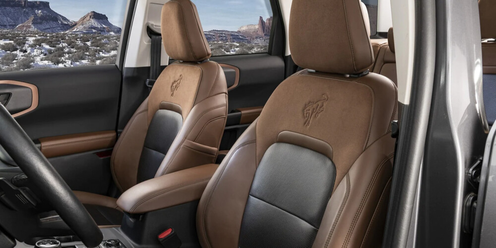 Brown leather car seats with embroidered logos, set in a vehicle interior against a snowy desert landscape visible through the windows. The scene conveys luxury and adventure.