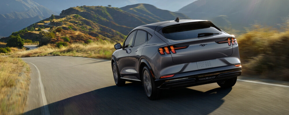 A sleek silver SUV with modern design drives on a winding mountain road surrounded by lush green hills. The scene is serene and adventurous.