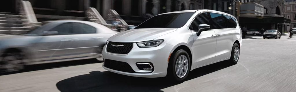 A white Chrysler Pacifica driving through a city street.