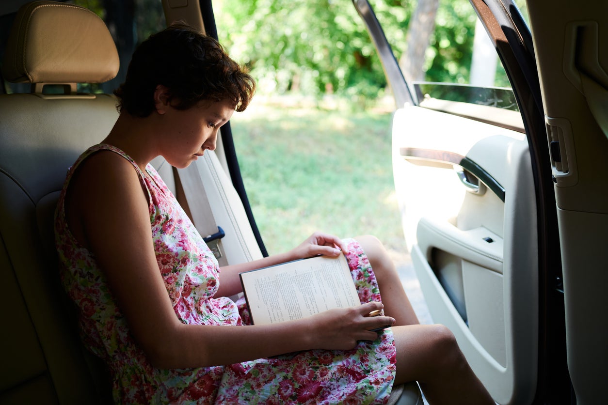Enthusiastic girl reading book in car in trip