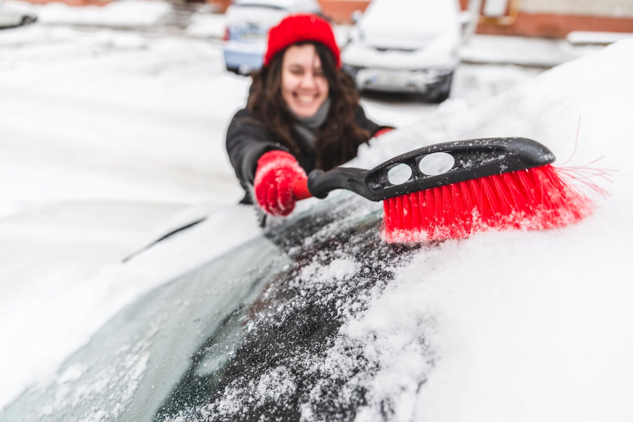 woman clean car with brush after snow