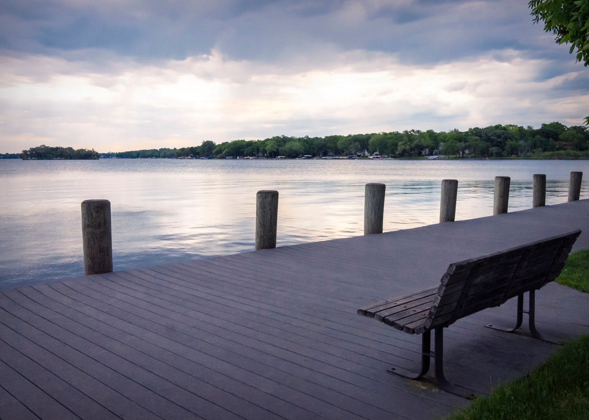 A lone bench looks out onto Pewaukee Lake in Waukesha County, Wisconsin, on a gray, cloudy morning.