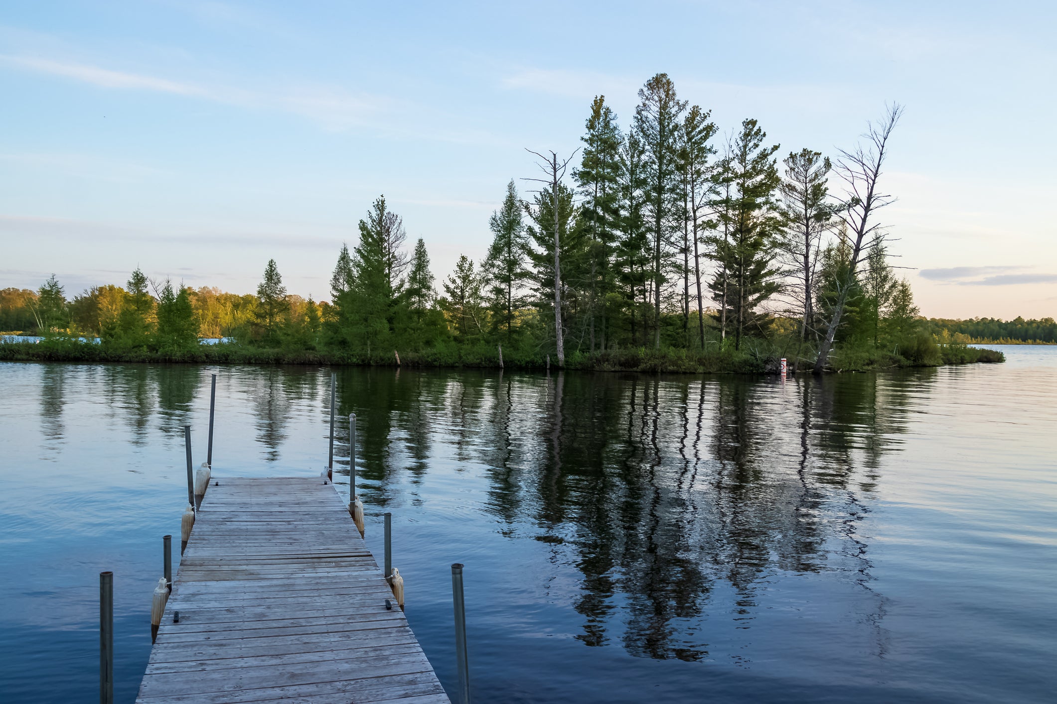 Pier jutting out into reflections of an island in the Chippewa Flowage near the shore of a Northwoods Forest park in Hayward, WI
