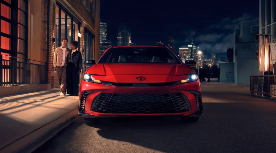 Front view of a vibrant red 2026 Toyota Camry parked along a downtown street at night with illuminated LED headlights, showcasing stylish 2026 Toyota Camry features for Waukegan IL commuters at Classic Toyota.