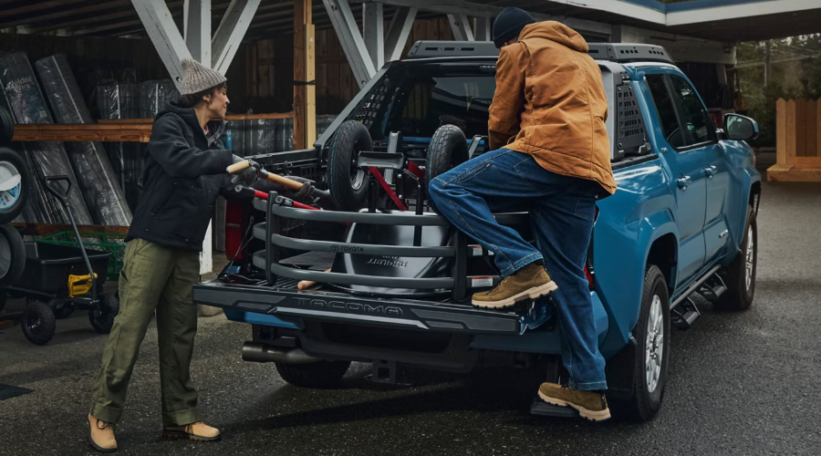 Two workers loading tools and equipment into the composite bed of a blue 2026 Toyota Tacoma truck using the bed extender on a damp morning job site in Waukegan, IL.