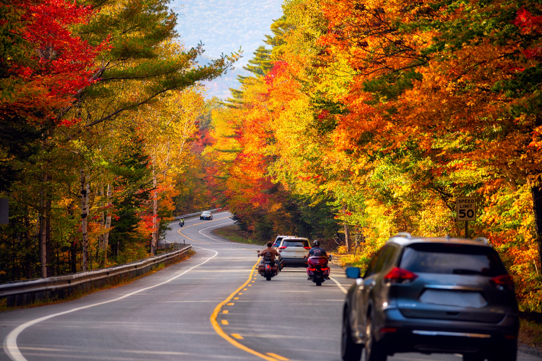Cars and motorcycles moving along a steep narrow road among a bright colorful autumn forest. USA.