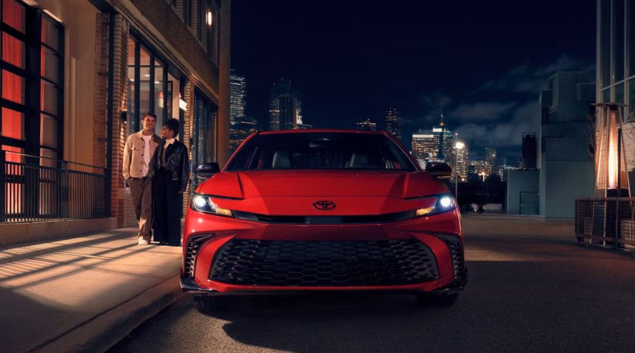 Front view of a red 2026 Toyota Camry showcasing its slim LED headlights and aggressive black sport grille at night in downtown Gurnee, IL.