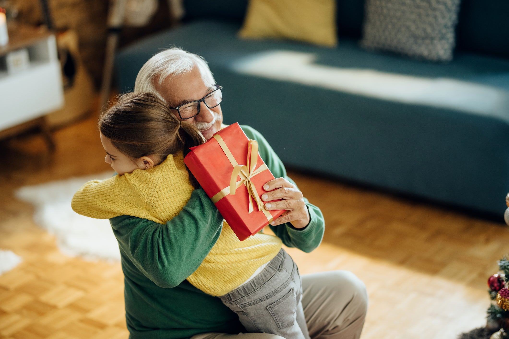 Grateful little girl embracing her grandfather while receiving Christmas present at home.