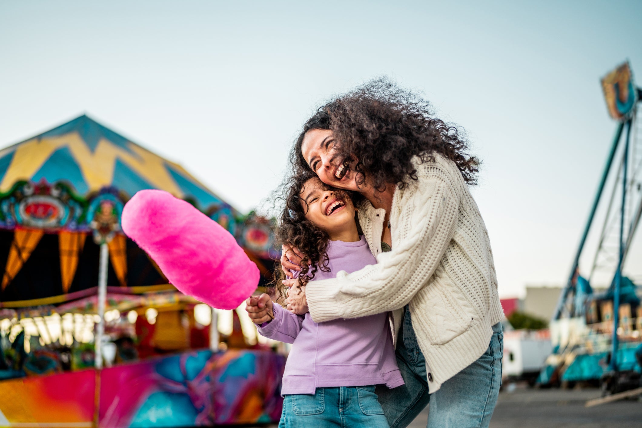 Child girl holding cotton candy and talking to mother at amusement park