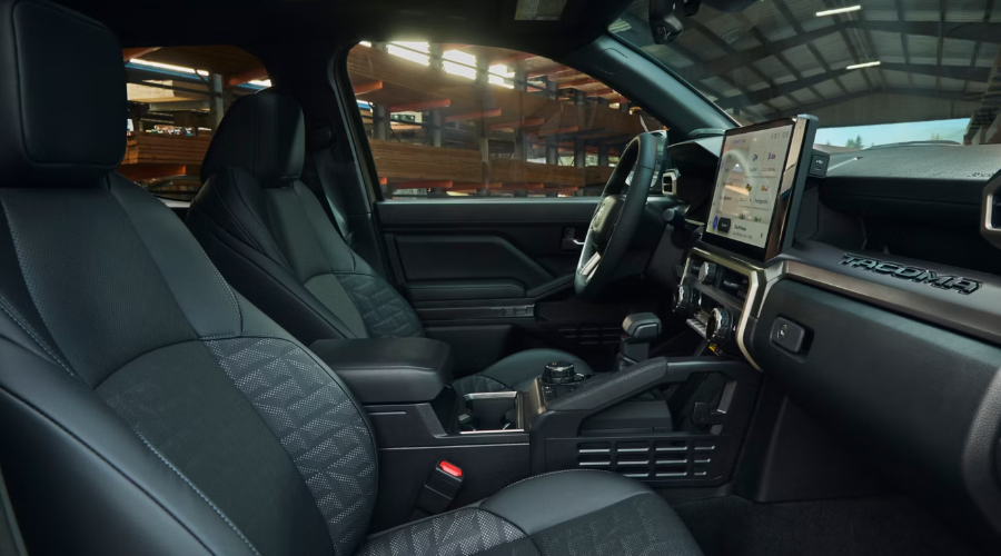 Side profile view of the 2026 Toyota Tacoma interior showing premium black seats, large touchscreen display, and center console controls parked outside a job site near Waukegan, IL.