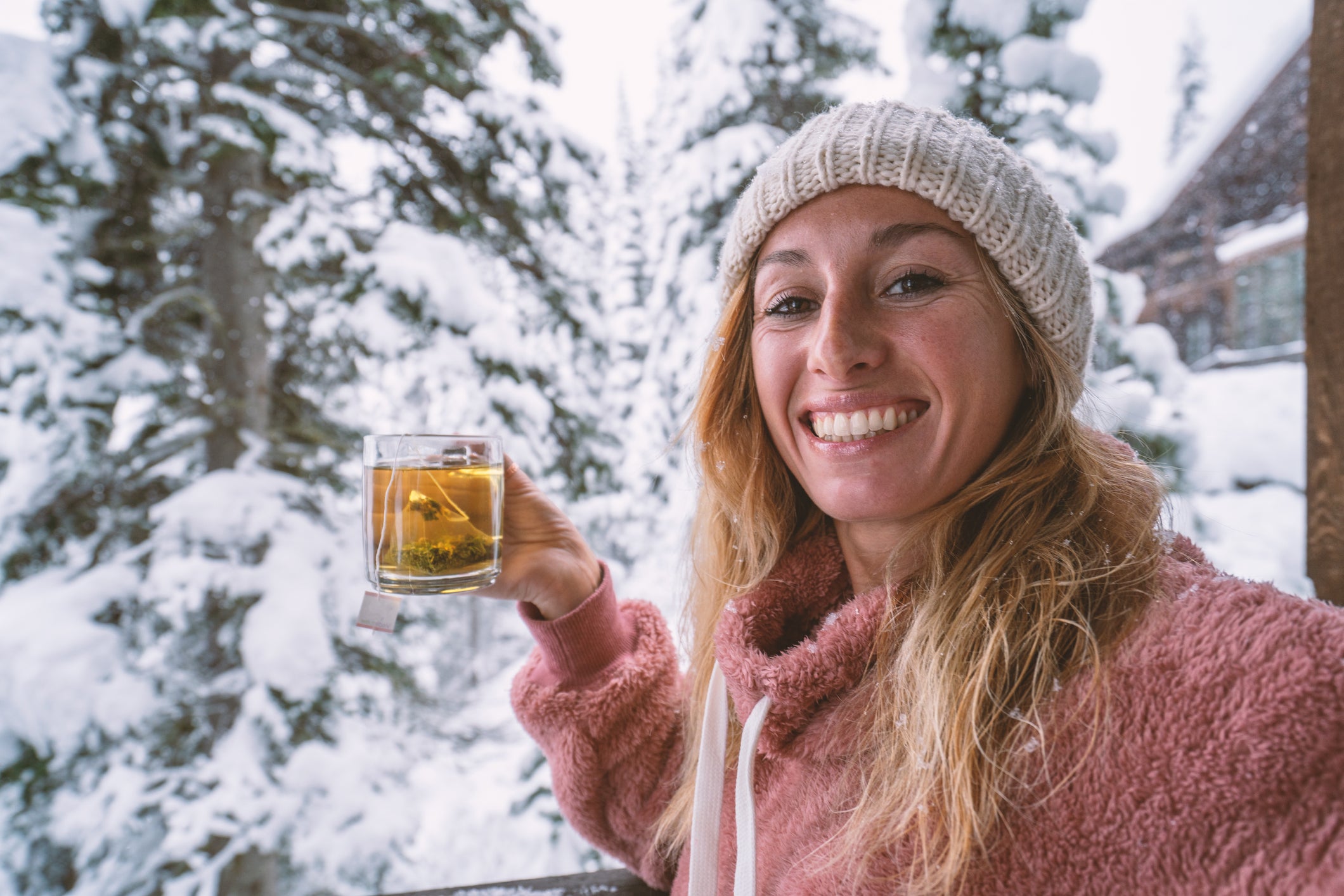 Woman in log cabine taking selfie with snow falling and tea cup in hands