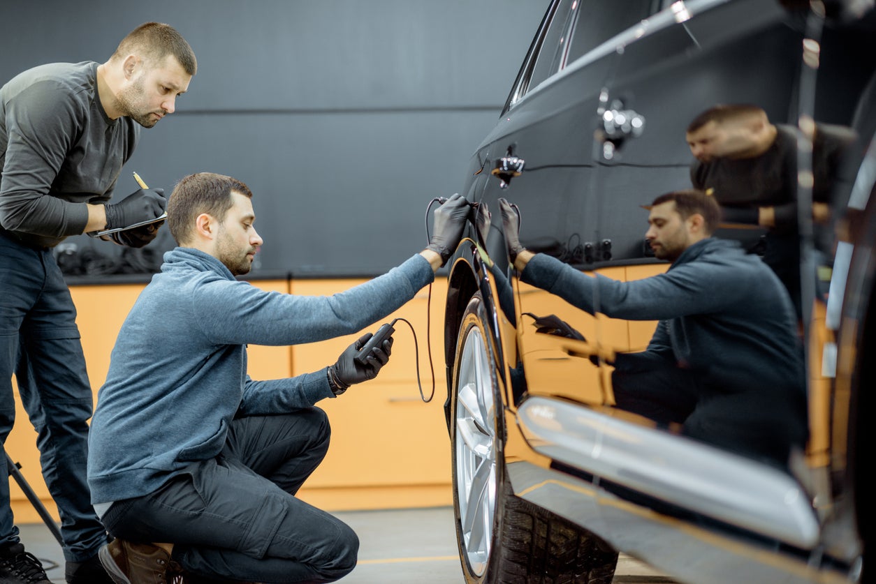 Workers examining vehicle body for scratches