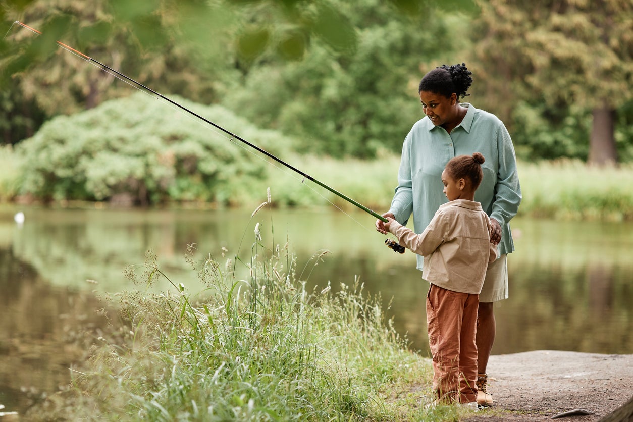 Side view caring black mother teaching little girl fishing