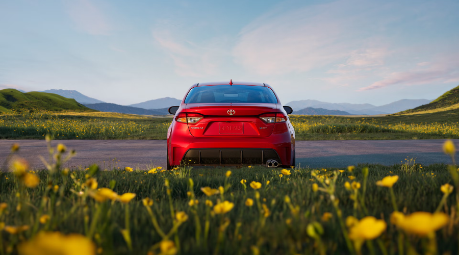 Rear view of a red 2027 Toyota Corolla hybrid sedan with LED taillights, lower rear diffuser, and dual exhaust tip parked along a scenic open road in Waukegan, available at Classic Toyota.