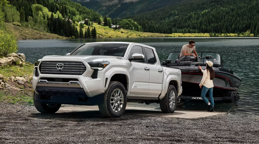 White 2026 Toyota Tacoma Limited pickup truck towing a fishing boat on a gravel boat ramp by a lake, demonstrating 4WD wet road traction and towing performance near Waukegan, IL.