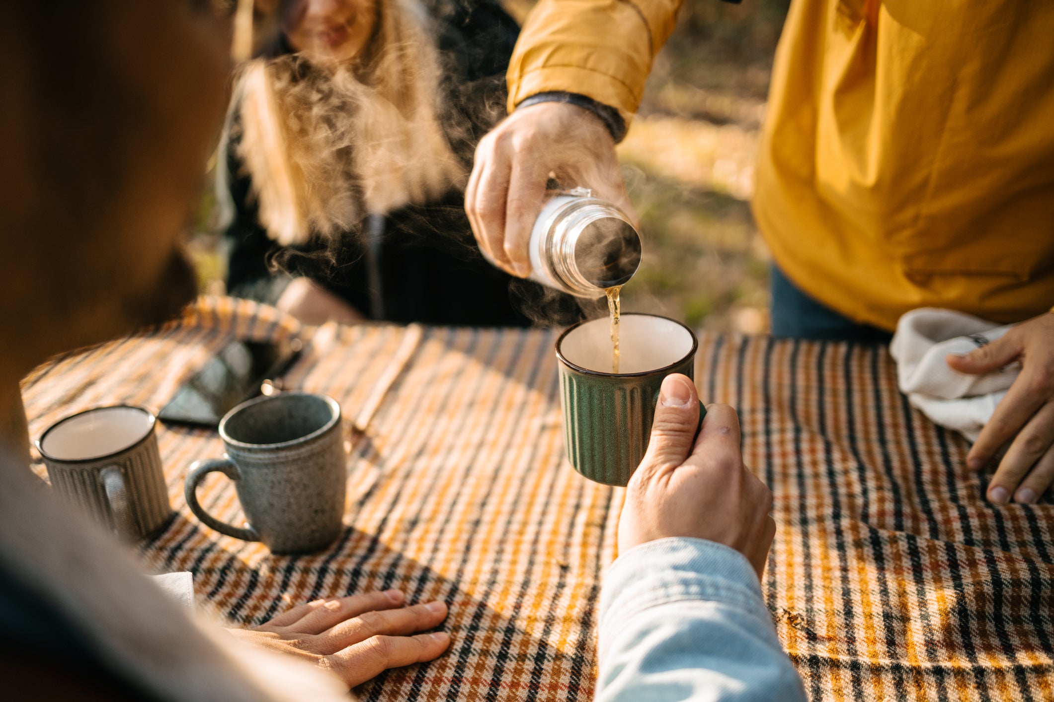 Group of campers pouring some tea into mug to warm up after a long hike outdoor