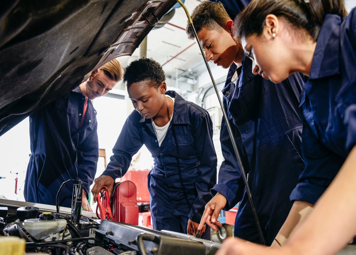 Group of student mechanics working on car engine with hood up