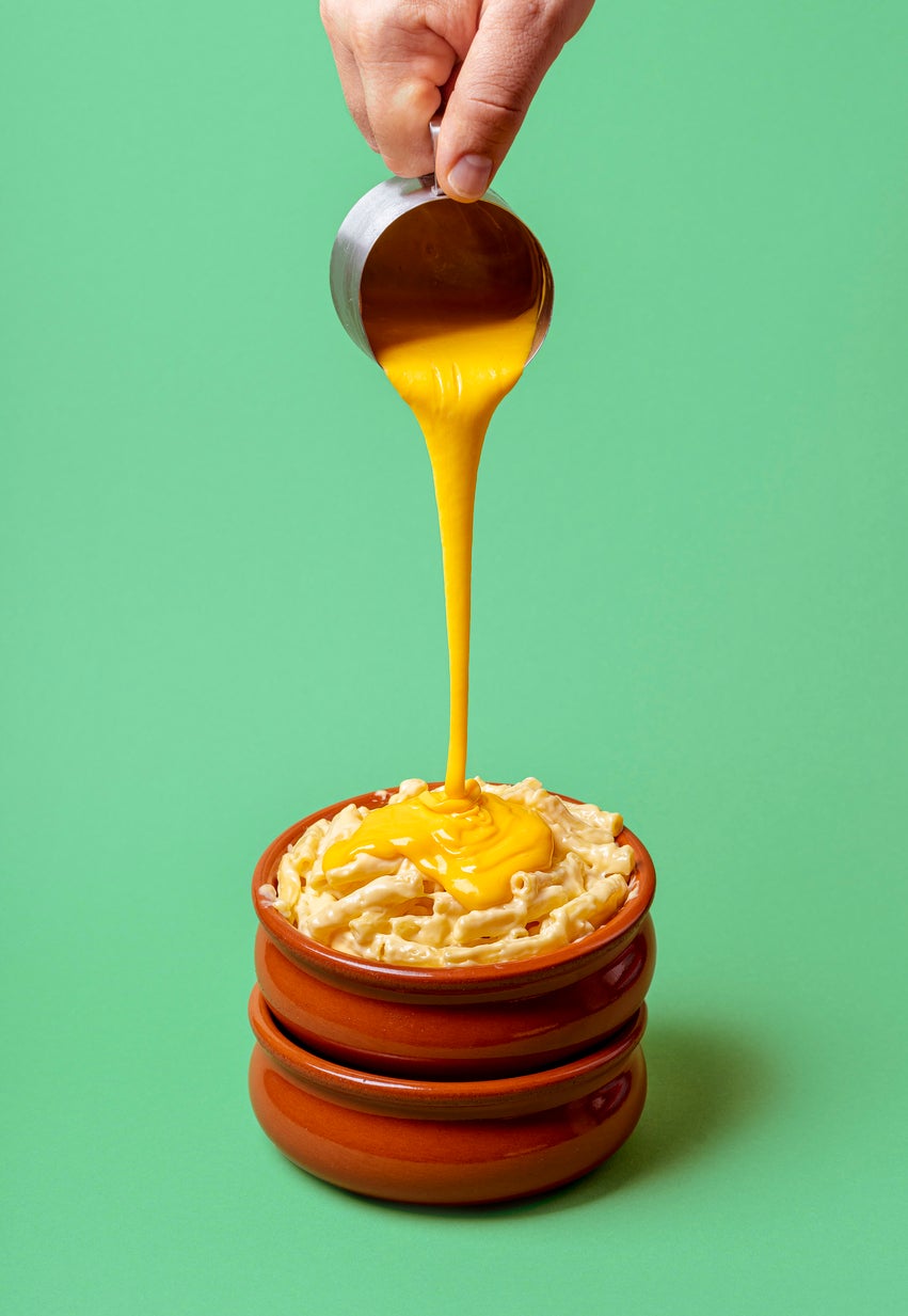 Macaroni and cheese making of. Pouring melted cheddar cheese over pasta.