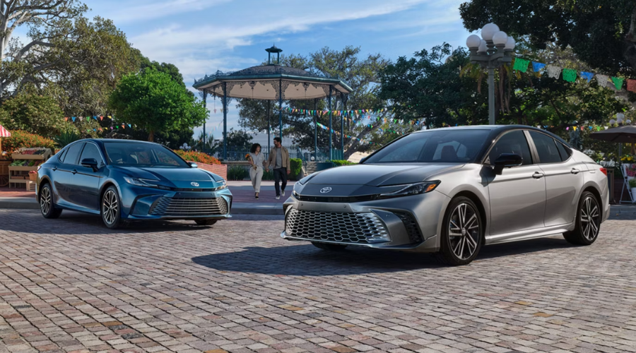 Two 2026 Toyota Camry hybrid sedans in blue and dual-tone silver parked near a brick plaza in Round Lake, IL, highlighting the redesigned front grilles 