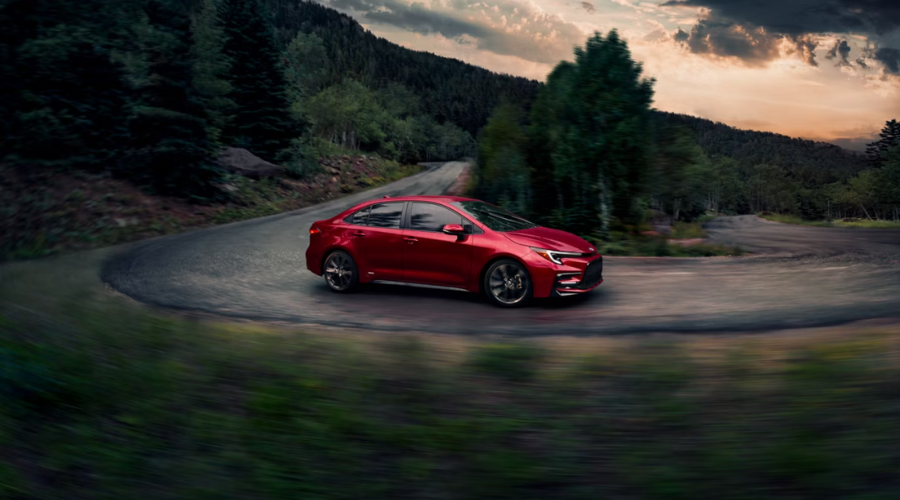 A red 2026 Toyota Corolla Hybrid navigating a curved road, highlighting the Electronic On-Demand AWD performance benefits for daily commuters in Waukegan and Gurnee, IL.
