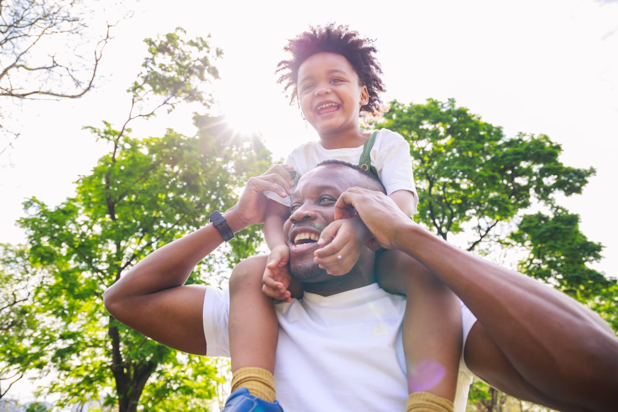 African American father giving son ride on back at park. family playing togetherness and relaxes. Family weekend. Cute African American boy with dad playing outdoor.
