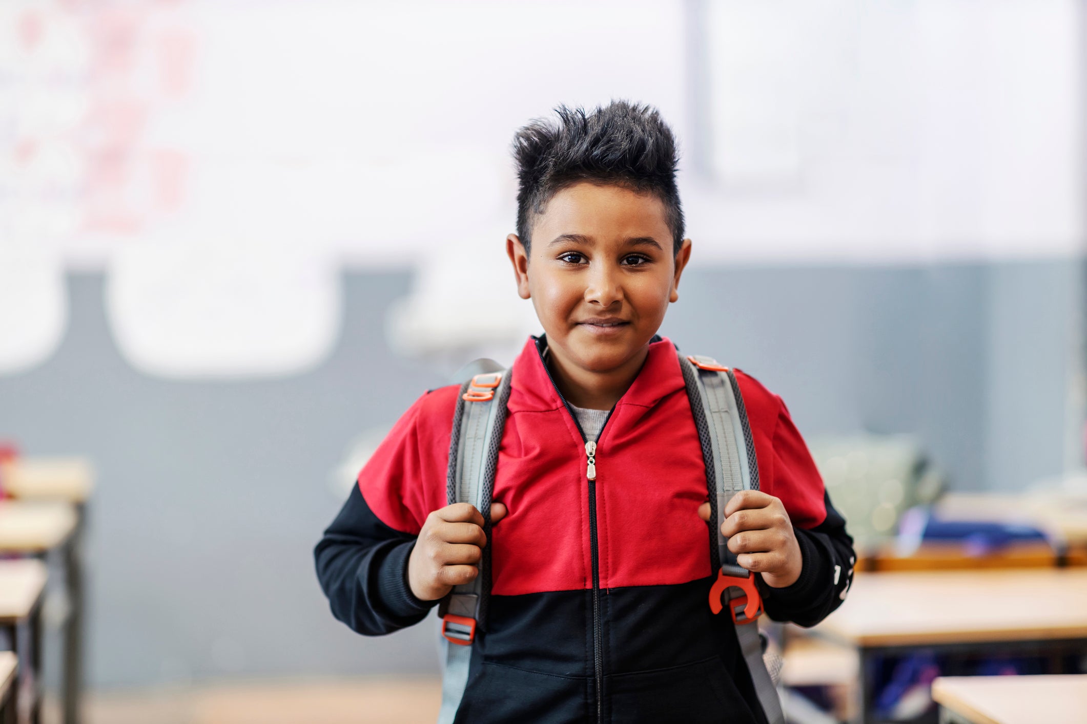 An Indian boy ready for school standing in classroom with backpack.