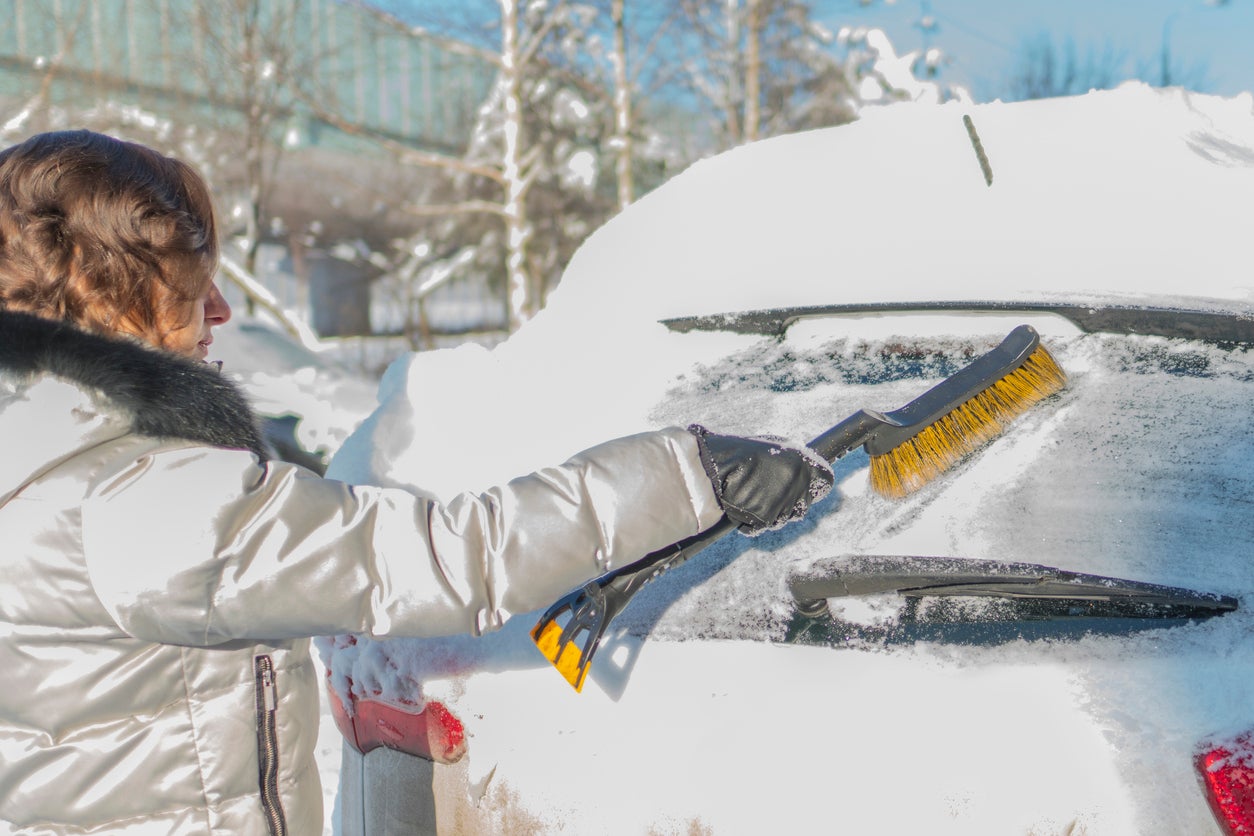 The girl is brushing the windshield of the car from the snow. Winter, day.