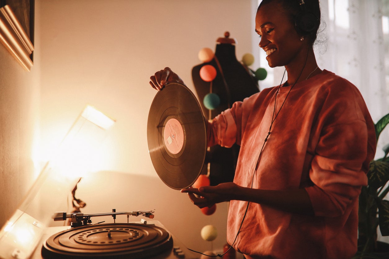 Young woman wearing tie dye shirt playing her record collection at home