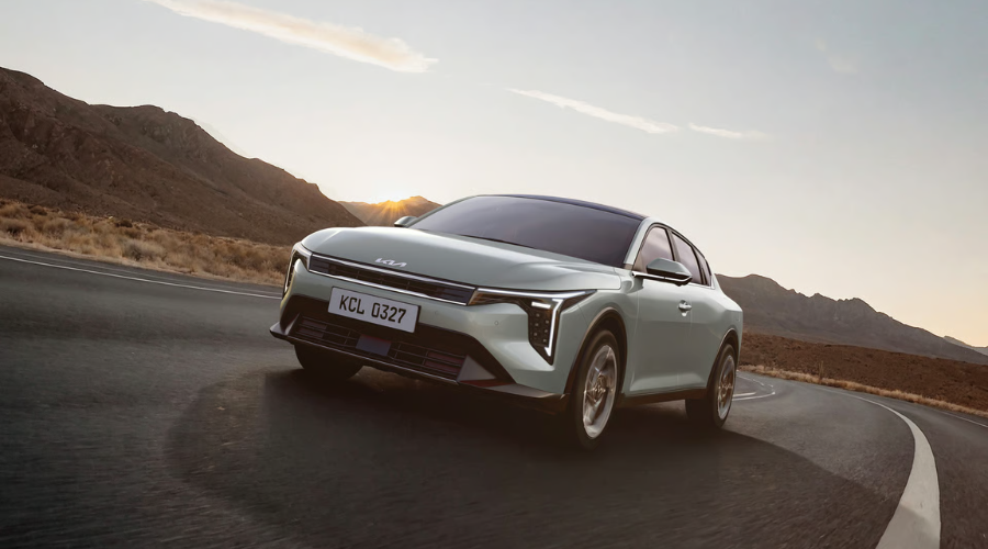 Front view of a 2026 Kia K4 fastback sedan with illuminated Star Map LED headlights navigating a road against mountain scenery, in stock at Classic Kia serving Waukegan and Lake County
