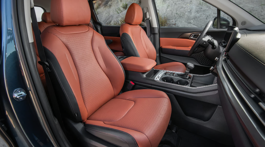 Front cabin interior of the 2027 Kia Carnival featuring terracotta brown and black perforated leather seats, center console, and modern dashboard tech available at Classic Kia near Waukegan, IL.
