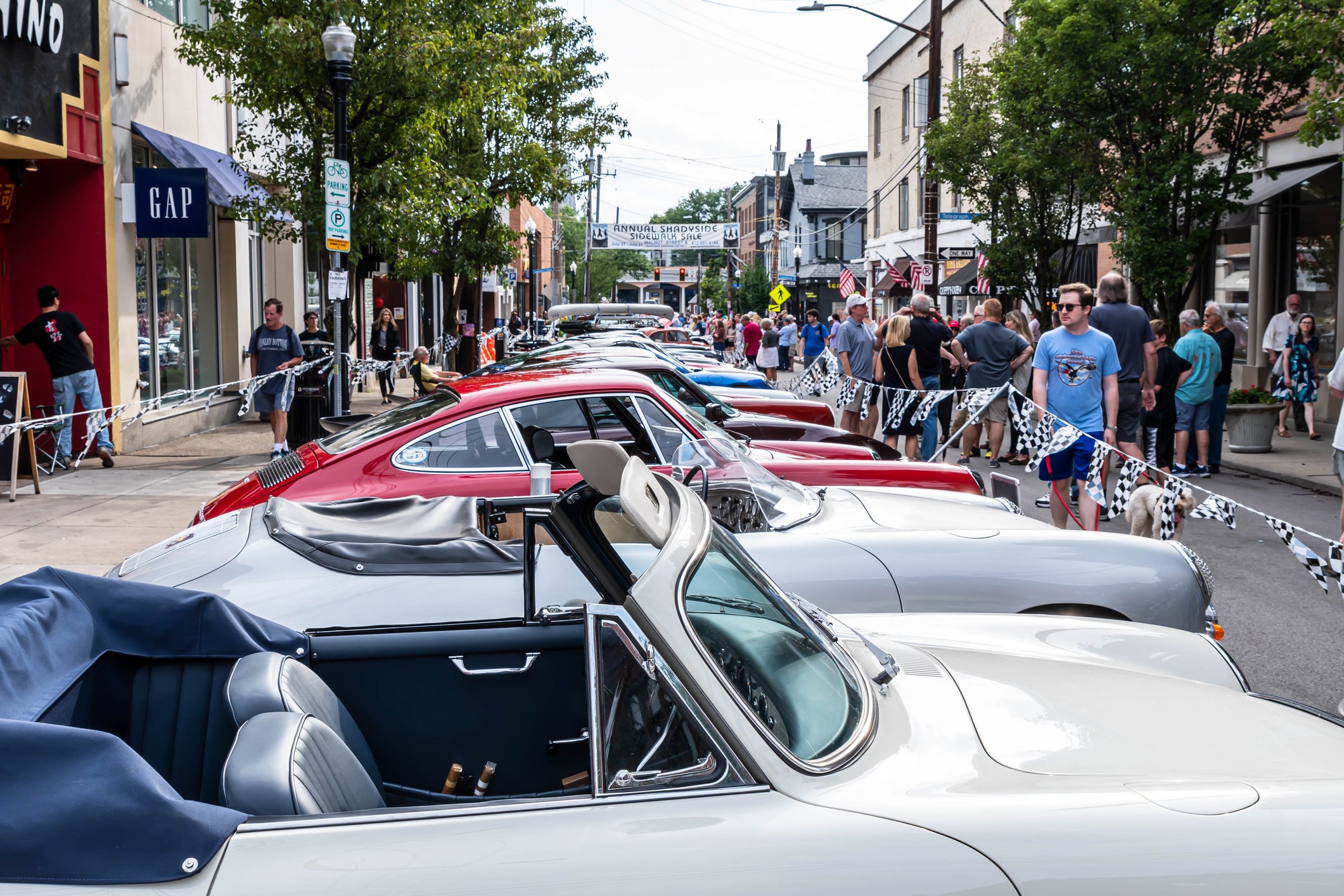 A car show in the Shadyside neighborhood with people walking along Walnut Street in Pittsburgh, Pennsylvania, USA