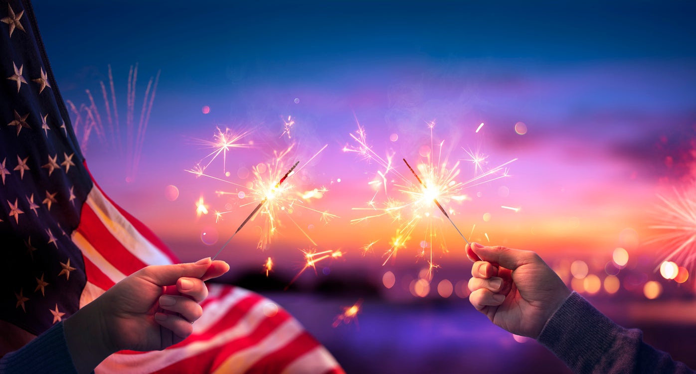 Usa Celebration With Hands Holding Sparklers And American Flag At Sunset With Fireworks