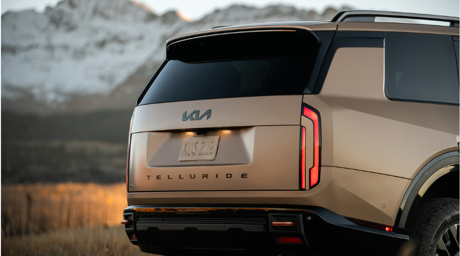 Rear tailgate view of a matte bronze 2026 Kia Telluride featuring vertical LED taillights, prominent block Telluride lettering, and automatic self-leveling rear suspension stance, set against a autumn mountain backdrop for fall camping trips across Waukegan and Lake County IL.