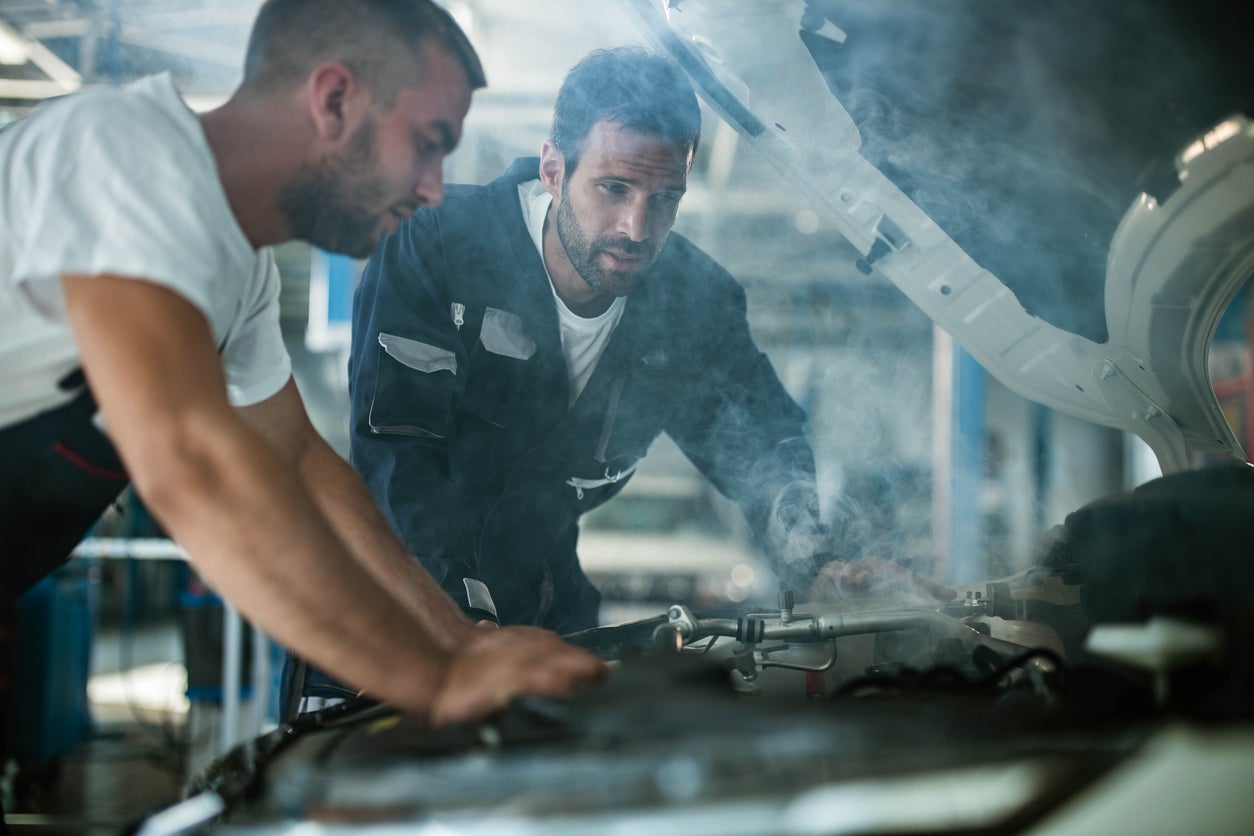 Auto mechanics working on overheated car engine in a workshop.