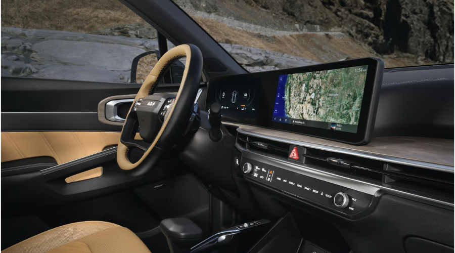 Angled driver-side view of the 2026 Kia Sorento interior featuring a curved panoramic dual-screen infotainment display with GPS navigation, a two-tone tan leather steering wheel, and physical climate control dials for easy navigation along I-94 and US-41 near Waukegan and Gurnee, IL.