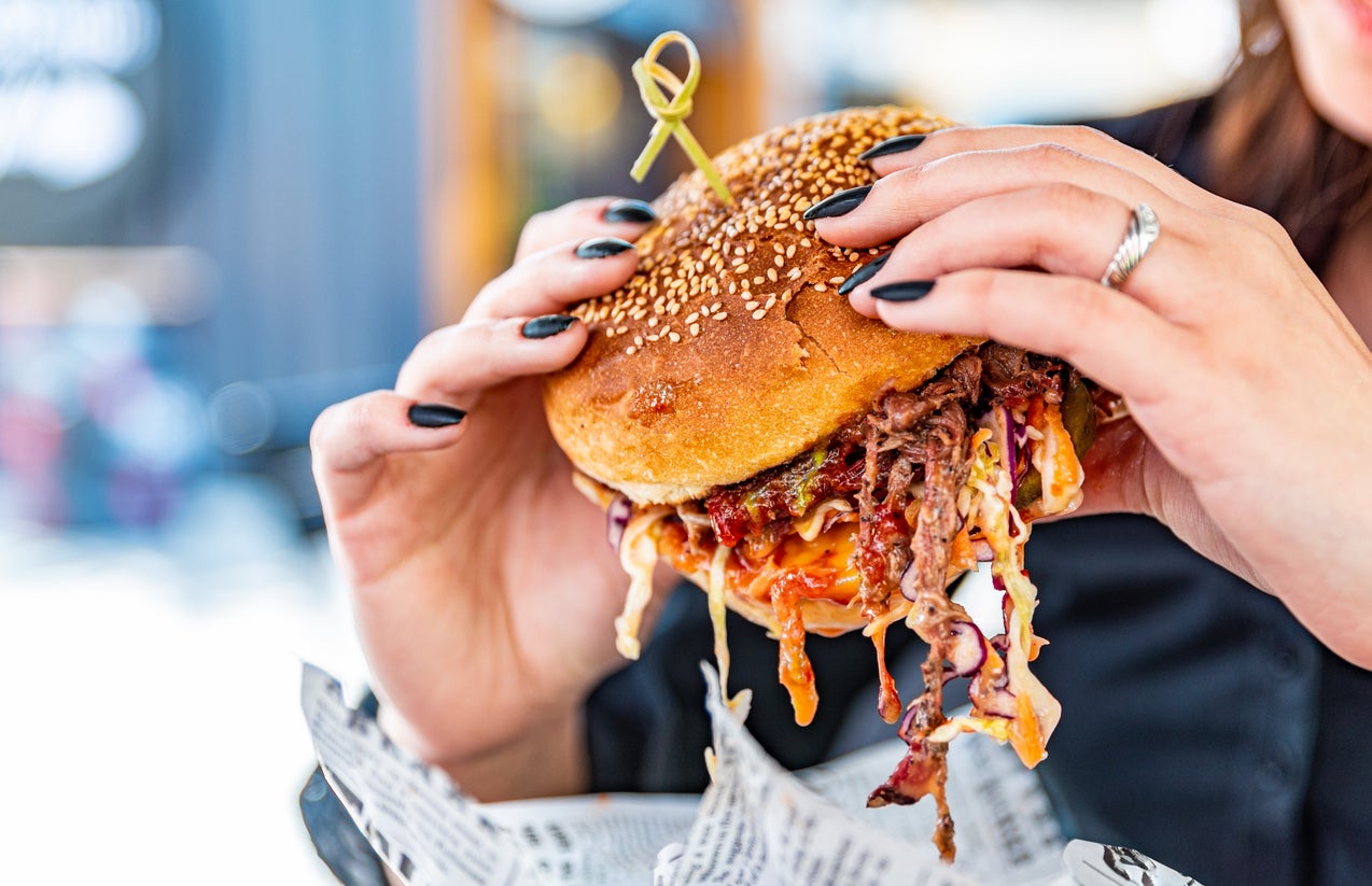 Woman eating street food burger outdoors. Traditional barbecue pulled beef burger with vegetables in woman hand