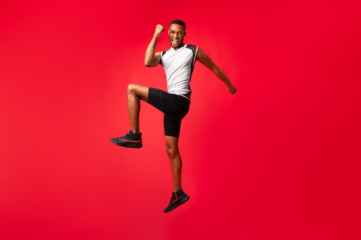 Full length afro guy celebrating success jumping at studio