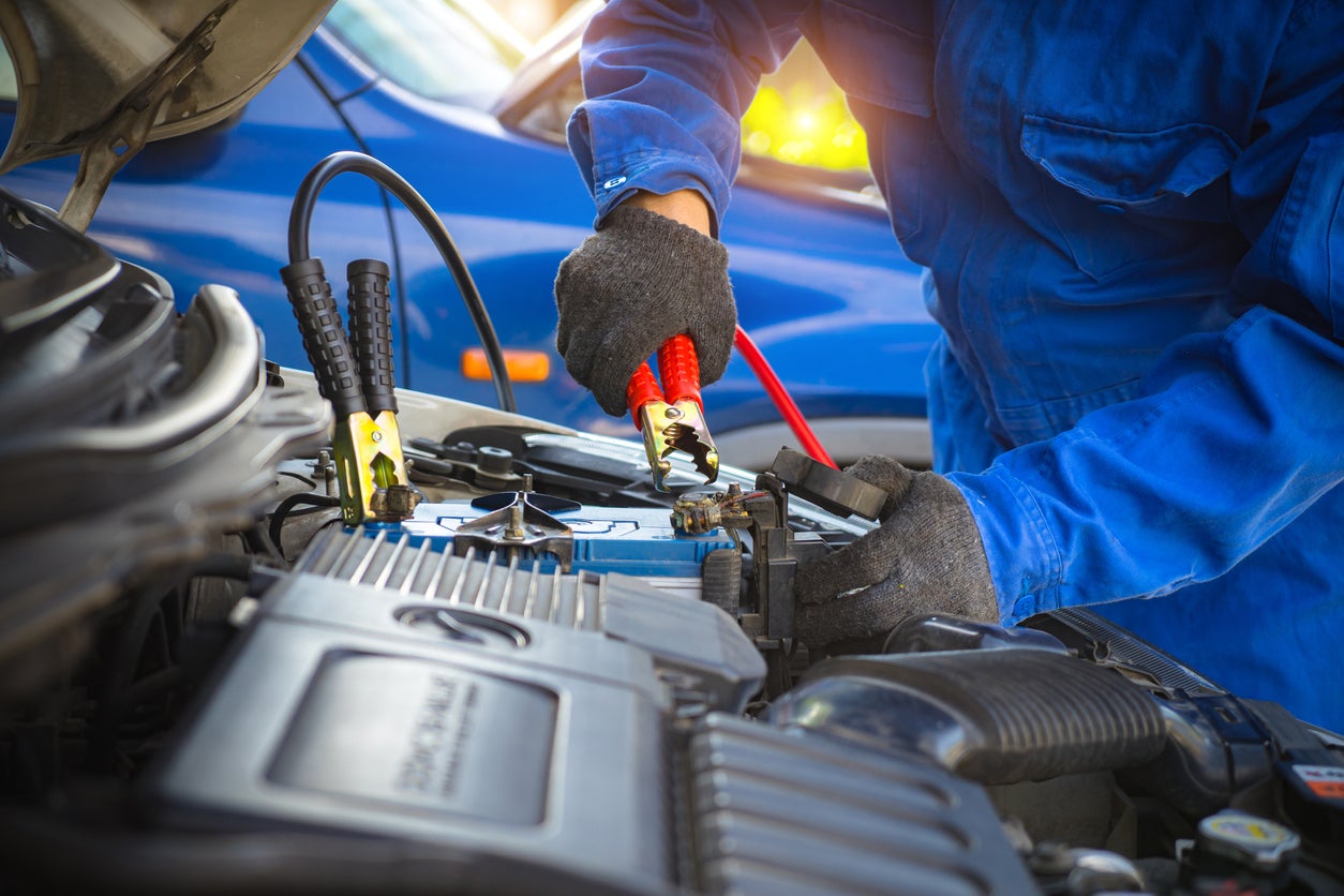 Battery car dead concept. A mechanic repair car battery, charging with red and black cables. fixing vehicle engine power down. Man holding jumper cable in garage.