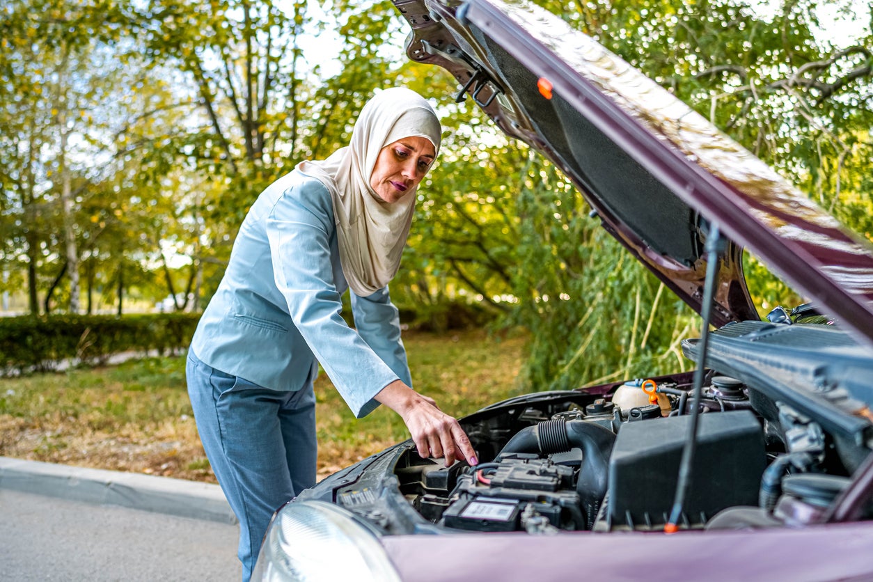 Mature Muslim woman looking at the engine of a broken car