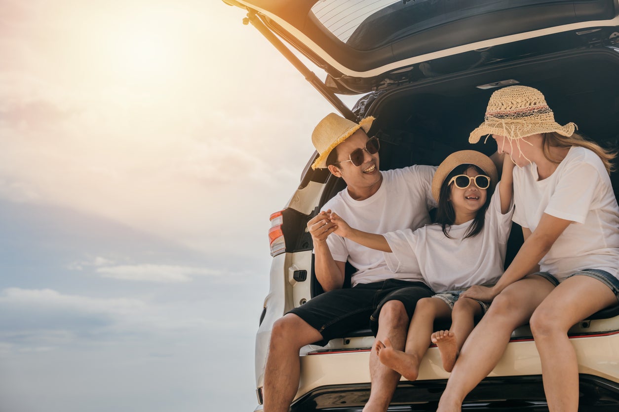 Dad, mom and daughter enjoying road trip sitting on back car