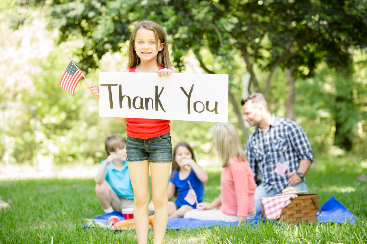 Child holds "Thank You" sign with American flag. Memorial Day.